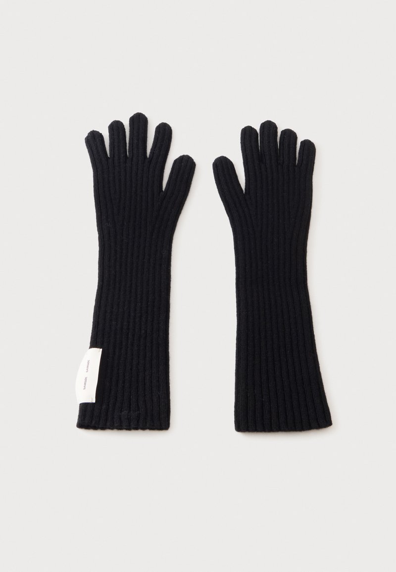 Paire de longs gants noirs en maille côtelée à cinq doigts avec une petite étiquette blanche en tissu sur un poignet, montrée à plat sur un fond clair.