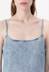 Denim gornji dio s podesivim tankim naramenicama, kvadratnim izrezom, svijetloplavim pranjem i suptilnim detaljima šivanja. Glatka, lagana tekstura.