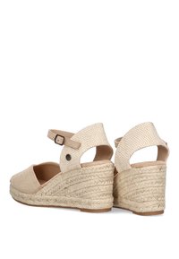 Sandalias de cuña beige con parte superior de tela texturizada, correa al tobillo con hebilla y plataforma trenzada de yute. Diseño de talón abierto con punta redondeada.