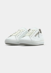 White sneakers with a smooth leather finish, flat laces, a side zipper, rubber sole, and minimalistic design. No visible patterns or accents.