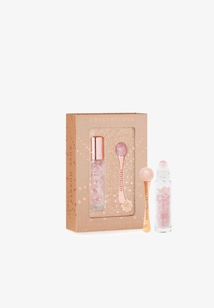 Set per la cura della pelle in quarzo rosa, in una scatola dorata e pesca. Include un rullo e una bottiglia con pezzi di cristallo rosa. Materiali lisci e lucidi.