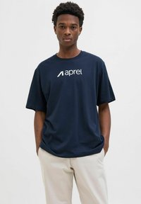 Marineblaue Baumwoll-T-Shirt mit einem weißen Markenlogo "aprel" auf der Vorderseite, kurzen Ärmeln und einem lässigen Schnitt. Kombiniert mit hellen Hosen.