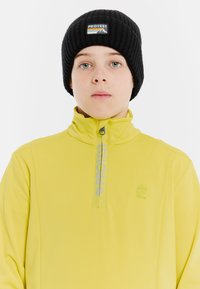 Geel half-zip pullover met een zachte textuur, voorzien van een grijs logo en een staande kraag. Zwarte geribde beanie met een patchaccent.