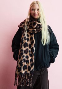 Šátek s leopardím potiskem z měkké látky, v odstínech béžové a tmavě hnědé. S třásněmi na koncích, spárovaný s černou oversized bundou.