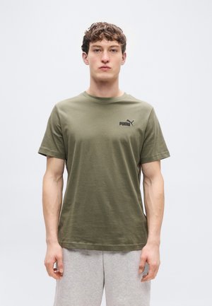 Camiseta de algodón verde oliva con cuello redondo, mangas cortas y un logo negro de Puma en el pecho. Modelo vistiendo pantalones deportivos grises.
