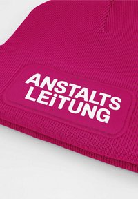 Fuchsia knit beanie with ribbed texture and a rectangular patch featuring the text "ANSTALTSLEITUNG" in bold white letters.