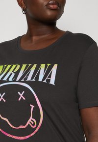 Melna kokvilnas T-krekliņš ar krāsainu "NIRVANA" grafiku virs smaidoša sejas designa. Ar apaļu kakla izgriezumu un brīvu piegriezumu.