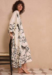 Długi, zwiewny kimono w kremowym materiale z czarnymi nadrukami kwiatów i ptaków. Posiada szerokie rękawy i luźny krój.