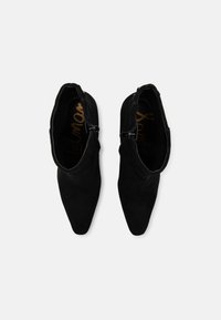 Botines de ante negros con punta afilada y cierre de cremallera. Textura suave, diseño minimalista, con un forro interior blando.