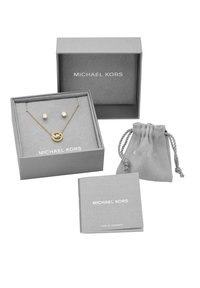 Guldfarvet halskæde med cirkulært vedhæng og glitrende øreringe i grå microfiber displaybokse, inkluderer garantihæfte og pose med snoretræk.