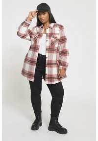 Różowa i biała koszula flanelowa w kratę z dwoma kieszeniami na piersi, z zapięciem na guziki i luźnym krojem, zestawiona z czarnymi obcisłymi dżinsami i botkami.
