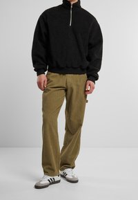 Sort fleece pullover med en kvart lynlås krave, parret med olivengrønne corduroybukser. Fodtøjet har hvide og grå nuancer med sorte striber.