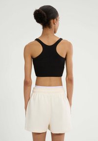 Czarny stanik sportowy z designem racerback, w połączeniu z kremowymi szortami z elastycznym pasem, które posiadają boczne kieszenie i luźny krój.