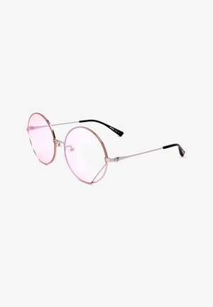 Occhiali da sole rotondi con lente rosa, sottili montature in metallo argento e terminali neri curvi, poggiati su una superficie bianca.