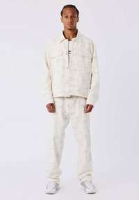 Veste en denim crème et pantalon avec un motif géométrique subtil. L'ensemble comprend une fermeture à boutons sur le devant et des poches standard.