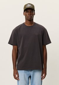 Γκρι βαμβακερό μπλουζάκι με κοντά μανίκια και στρογγυλή λαιμόκοψη. Φέρει μικρό λογότυπο "LES DEUX" στο στήθος. Συνδυάζεται με ανοιχτόχρωμο τζιν παντελόνι και πράσινο καπέλο.