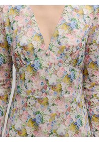 Ein blumig gemustertes Kleid mit tiefem V-Ausschnitt, langen Ärmeln und strukturiertem Stoff in Rosa-, Blau- und Gelbtönen. Knöpfe betonen den Taillenbereich.