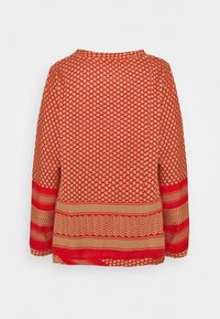 Rode top met lange mouwen met geometrische patronen, voorzien van een gestructureerd gebreid materiaal en gestreepte accenten bij de manchetten en zoom. Ronde halslijn.