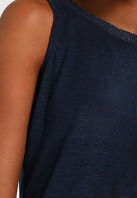 Närbild av en person som bär en ärmlös mörkblå topp med en subtil strukturerad tyg.