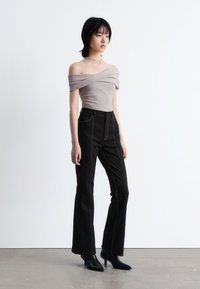 Beige Off-Shoulder-Oberteil mit drapiertem Stoff, kombiniert mit hochgeschnittenen schwarzen, ausgestellten Jeans mit kontrastierenden Nähten und spitzen schwarzen Absätzen.