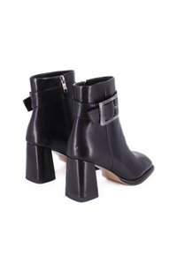 Stivaletti neri in pelle con punta quadrata, tacco spesso, zip laterale e fibbia decorativa sulla cinghia a caviglia. Texture liscia.