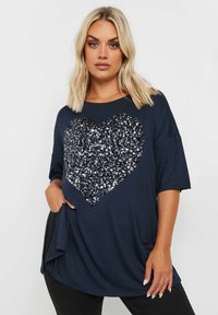 Marinblå t-shirt med ett stort hjärtformat paljettmönster i silver och marinblått. Korta ärmar, lös passform och sidfickor. Slät tygkvalitet.