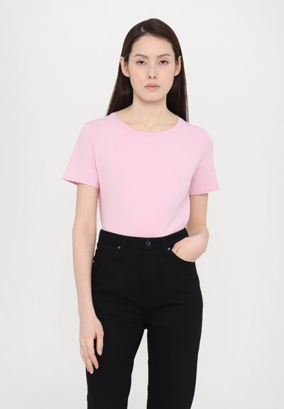 Lys rosa t-skjorte med korte ermer og rund hals, kombinert med svarte høyhårede bukser. Stoffet ser glatt og tettsittende ut.