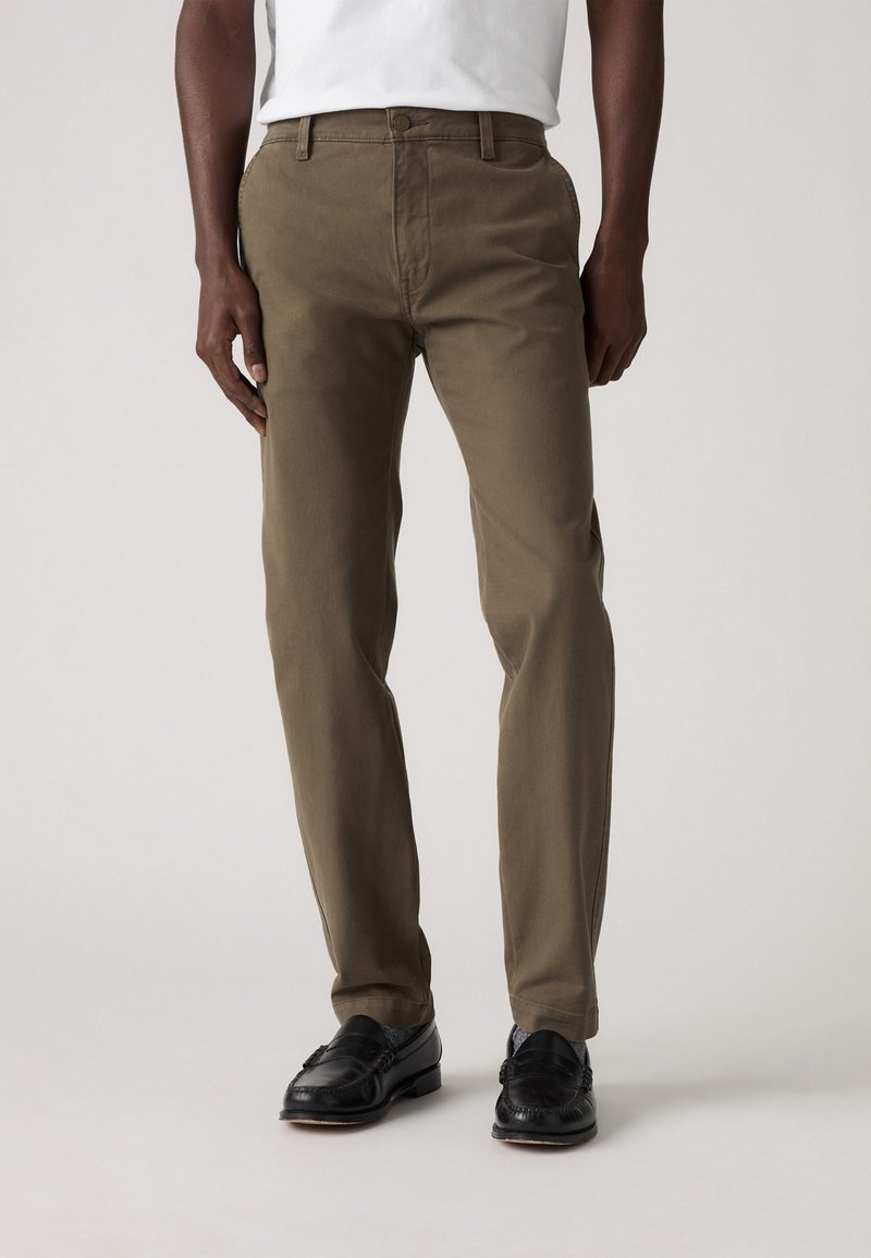 Khaki cotton trousers with a straight fit, visible front pockets, and a button closure. Paired with black loafers and a white top.