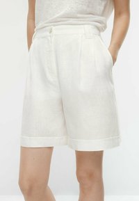 Hvide linned shorts med skræddersyet design, der har knaplukning, sidelommer og opsmøg ved kanten. Glat tekstur, knælang.