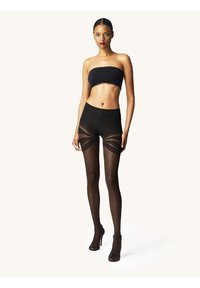 Sorte gennemsigtige strømpebukser med høj talje. Har stribede udskæringsdetaljer på lårene. Modellen bærer en sort off-shoulder top og hæle.