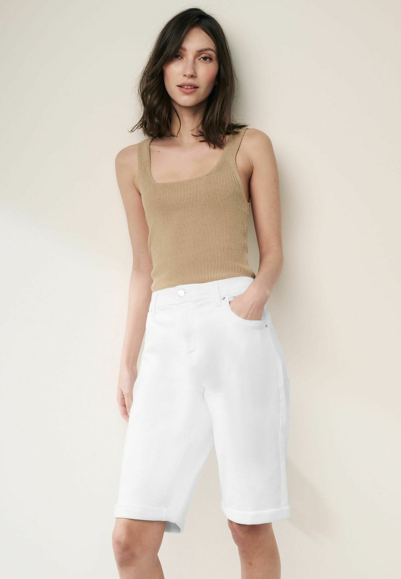 Beige ribbad topp med breda axelband, kombinerad med vita denimshorts med uppvikta ärmar, frontfickor och en avslappnad passform.