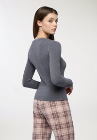 Maglietta grigia a maniche lunghe in tessuto a coste, con taglio aderente e scollatura a girocollo, abbinata a pantaloni rosa a quadri.