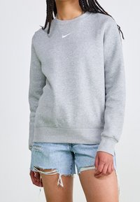 Grå crewneck sweatshirt med ribbade ärmslut och fåll, med en liten vit Nike-logotyp på bröstet. Bärs med slitna denimshorts.