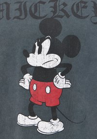 Grafické tričko s Mikym Mousem v černé a červené barvě, s opotřebovanou texturou, na tmavě šedé látce. Text nahoře zní "Mickey."