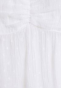 Tissu blanc texturé avec de subtils points en relief et des plis, présentant un corsage froncé, design léger et aéré.