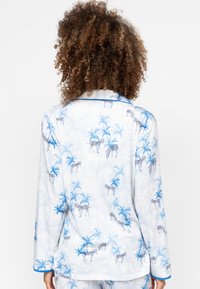 Witte pyjama top met een blauwe palmboom en zebra-print. Heeft lange mouwen en blauwe piping langs de kraag en manchetten.