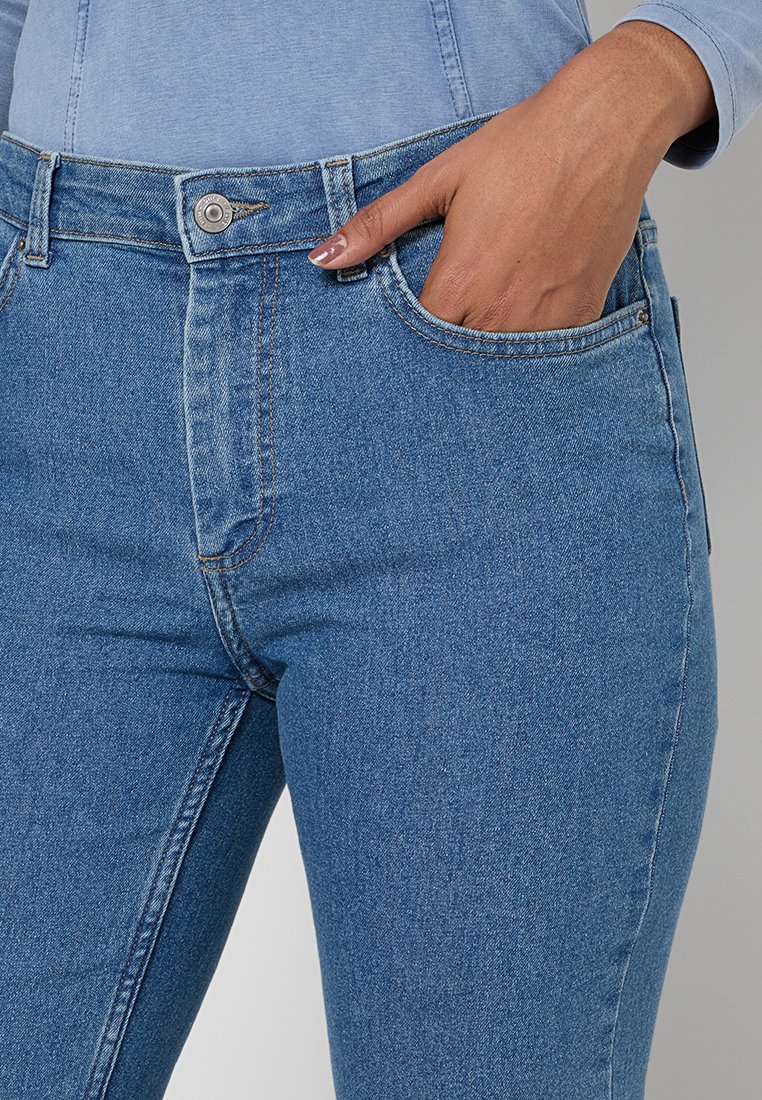 Blauwe denim jeans met een getailleerd ontwerp, voorzakken en een zilveren knoopsluiting. De stof heeft een klassieke textuur met een lichte vervaging.