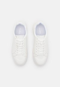 Zapatillas blancas con empeine sintético suave, puntera redonda y cordones planos. Cuentan con un cuello acolchado y una plantilla acolchada. Logo de la marca visible.