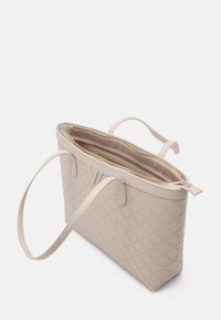Beige quilted tote bag with dual handles, zip closure, and smooth interior lining. Features a structured shape and subtle hardware accents.