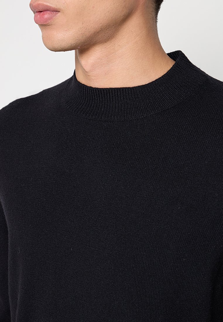 Schwarzer Strickpullover mit Rundhalsausschnitt, der eine glatte Textur und eine figurbetonte Passform aufweist. Keine sichtbaren Muster oder zusätzlichen Akzente.