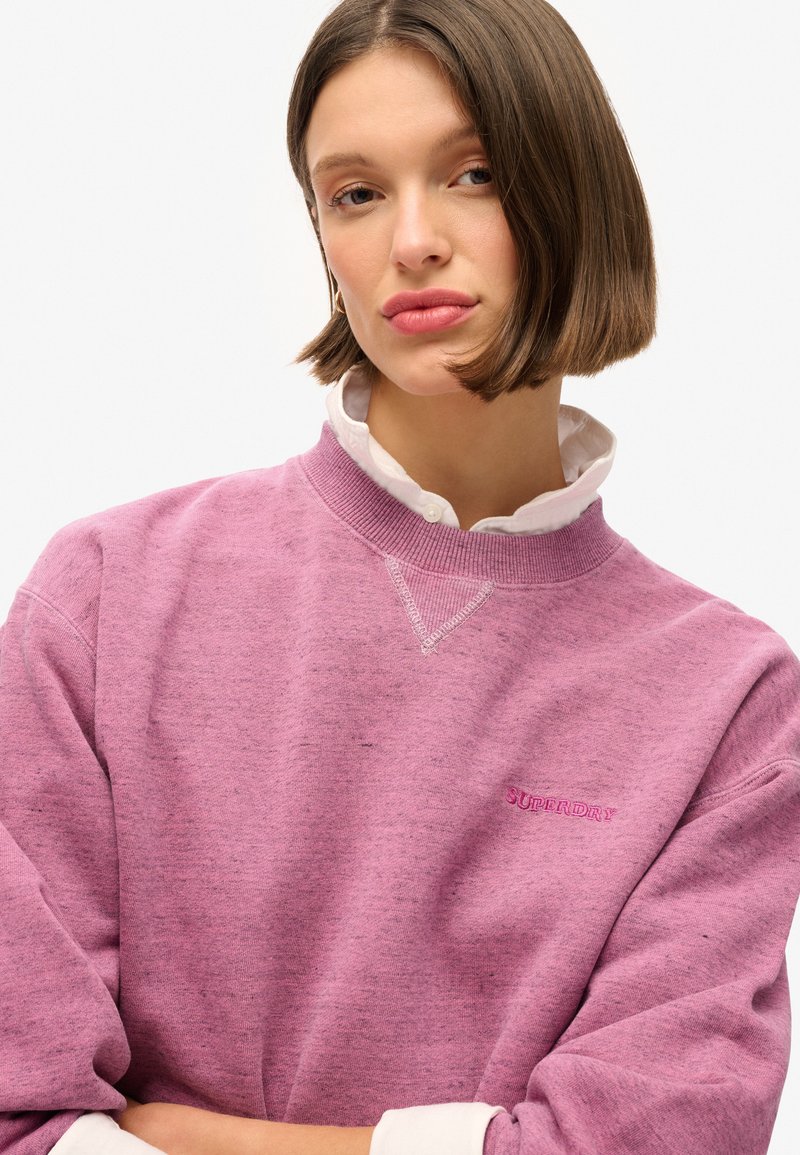 Felpa viola chiaro con colletto a costine, caratterizzata da un logo sottile in viola scuro. Tessuto morbido e vestibilità rilassata.