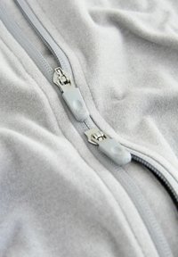 Graues Fleecegewebe mit einem durchgehenden Reißverschluss. Verfügt über graue Reißverschluss-Ziehen und metallische Reißverschluss-Zähne. Glatte Textur mit subtiler Glanz.