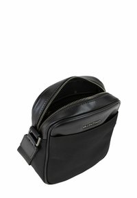 Sac bandoulière noir avec un corps en tissu texturé et des accents en cuir lisse. Comprend une fermeture éclair sur le dessus et un détail de logo à l'avant.