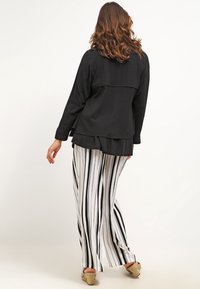 Black long-sleeve top with layered design, paired with flowy white pants featuring vertical black stripes. Textured material; simple accents.