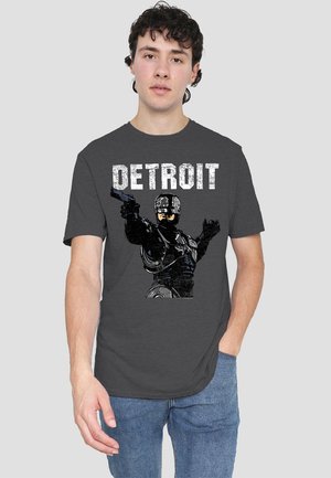 Gray t-shirt featuring a black graphic of a figure holding a gun, with the text "DETROIT" above in bold white distressed font.