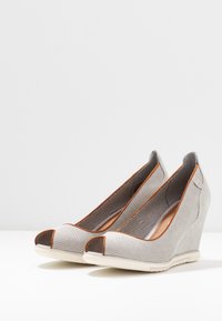 Scarpe con zeppa con una parte superiore perforata grigia, accenti marroni e design aperto sulla punta. Il tacco in zeppa è grigio chiaro con una finitura testurizzata.