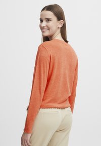 Pulover tricotat portocalie cu mâneci lungi, decolteu rotund și un croi lejer. Purtați cu pantaloni bej, evidențiind o textură interesantă.