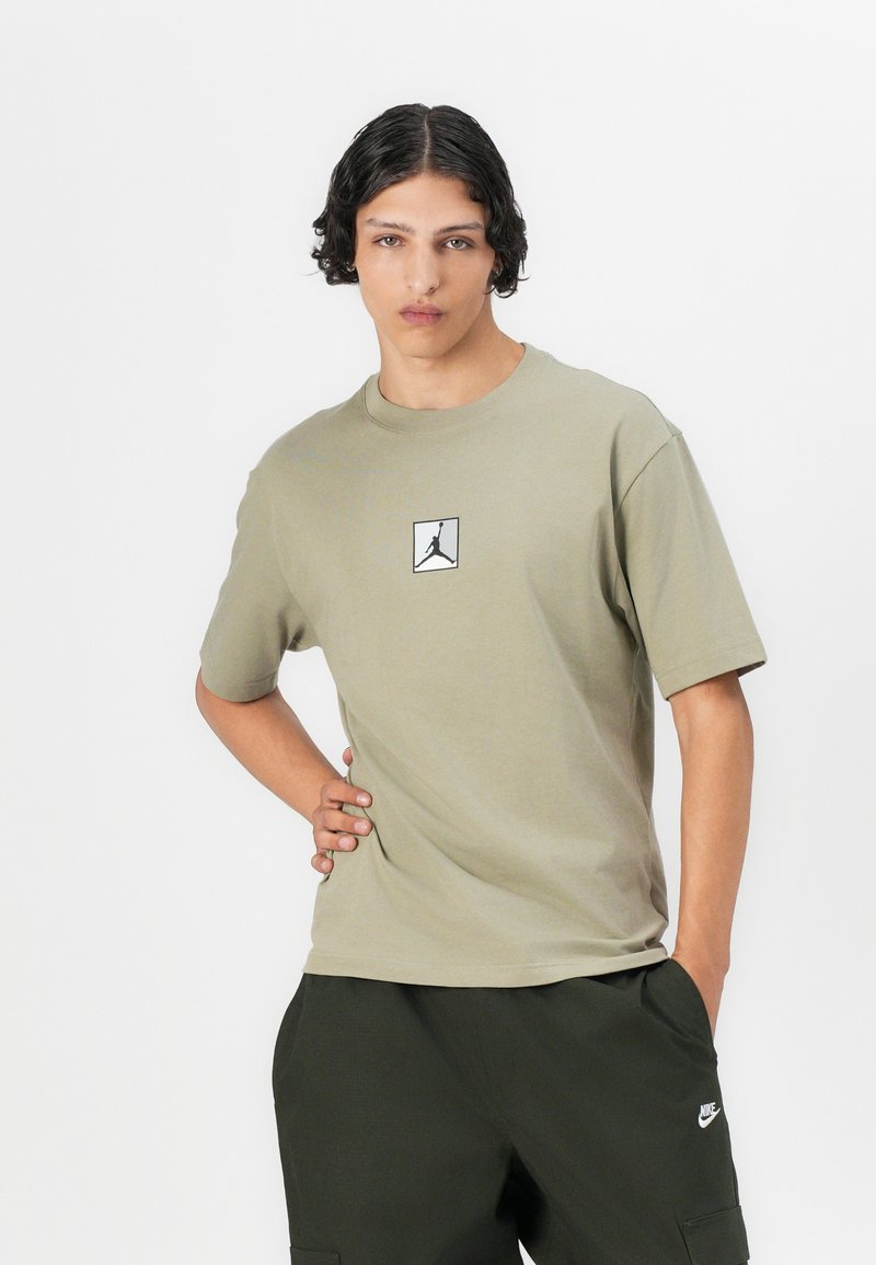 T-shirt en coton vert olive à manches courtes, arborant un petit logo Jordan noir et blanc. Texture lisse, coupe décontractée, encolure ronde.