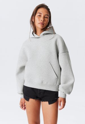 Gray oversized hoodie made from soft fabric with a kangaroo pocket and a drawstring hood, paired with black distressed shorts.