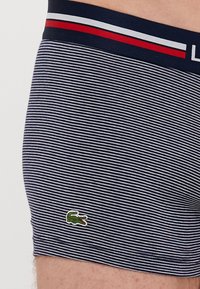 Gestreifte Boxershorts in Marineblau und Weiß mit einem kontrastierenden Bund in Rot, Weiß und Blau; verfügt über ein kleines gesticktes grünes Krokodil-Logo.